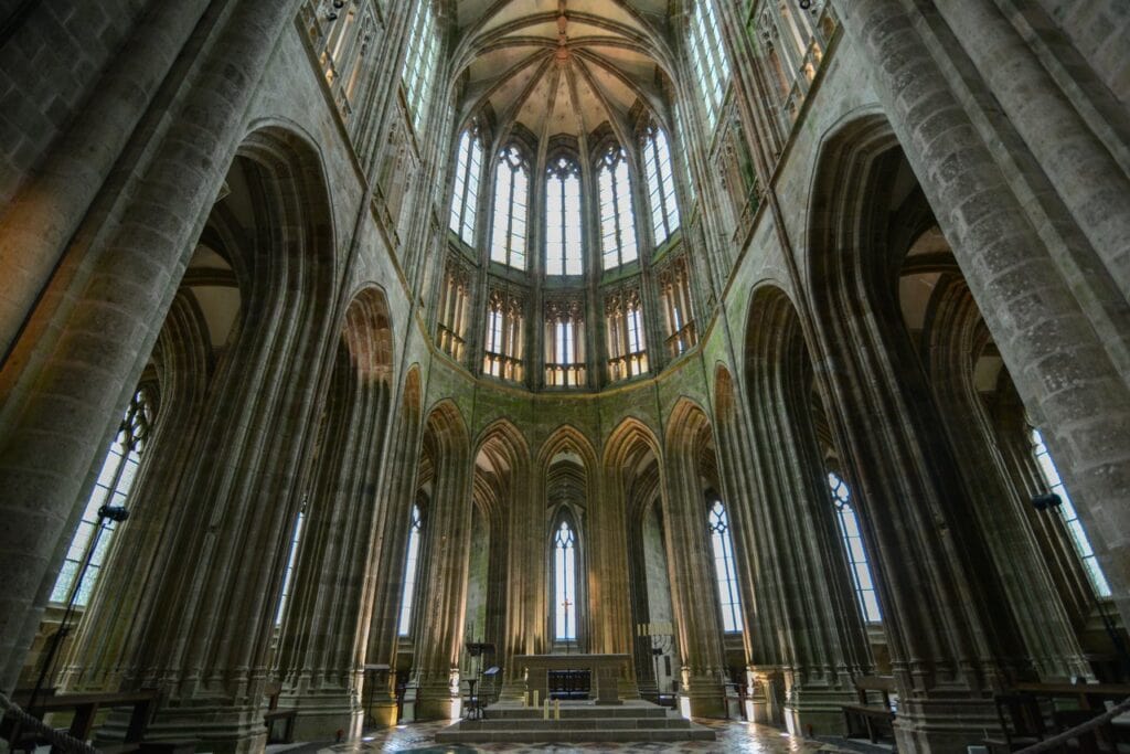 Mont-Saint-Michel 11 The Gothic choir of Mont-Saint-Michel abbey church seen from the crossing, a polygonal apse ringed by an ambulatory, two tiers of traceried windows above it, and stone rib vaults throughout.