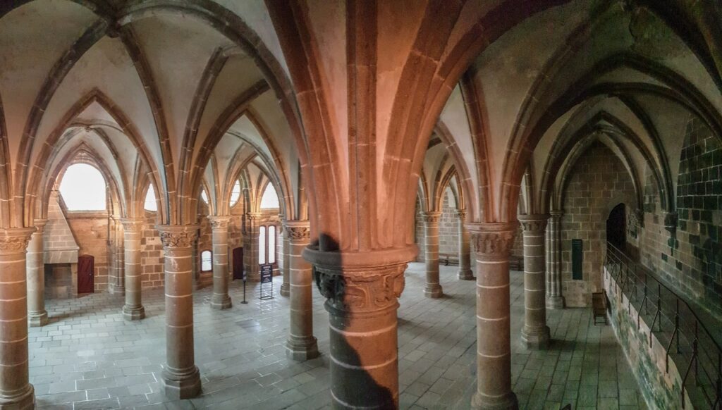Mont-Saint-Michel 16 A large Gothic hall with heavy clustered columns and ribbed vaults, warmly lit