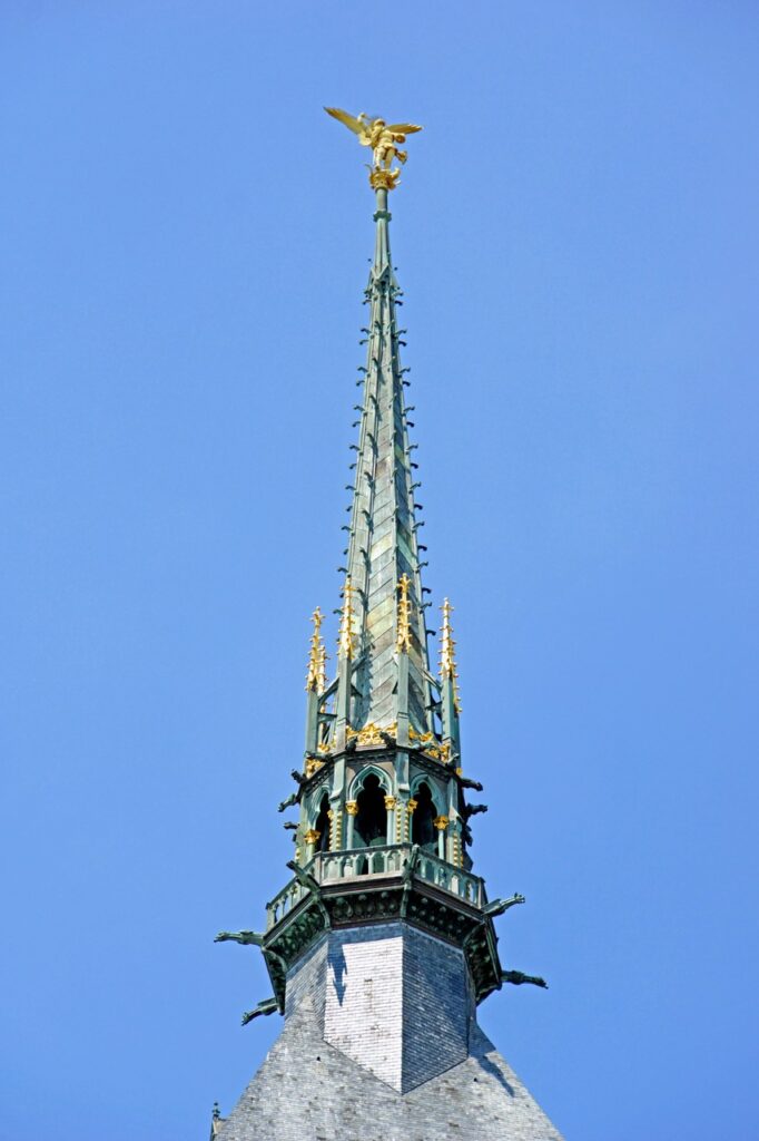 Mont-Saint-Michel 23 A gilded statue of Saint Michael on top of a slender neo-Gothic stone spire against a blue sky