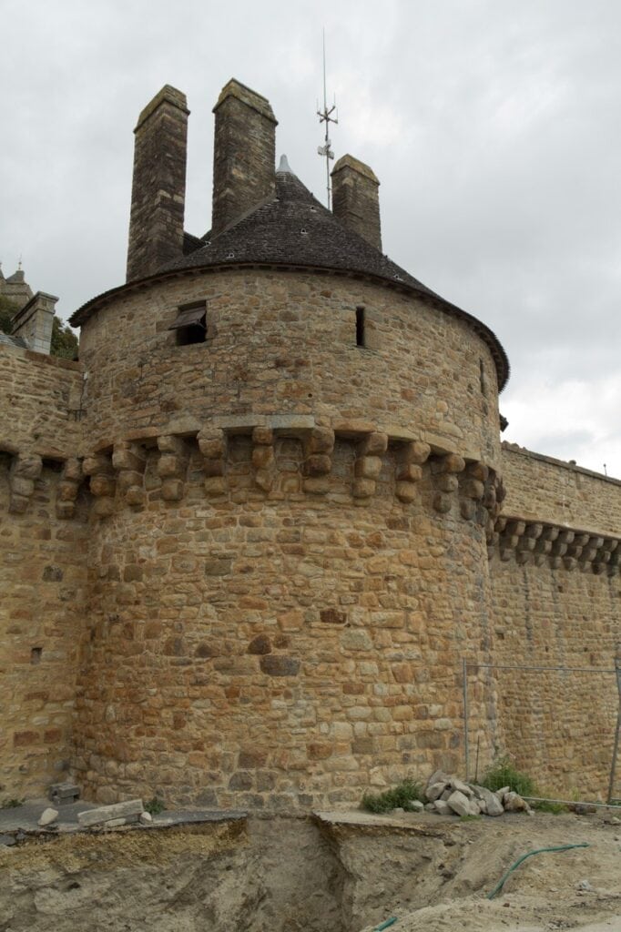 Mont-Saint-Michel 7 A round stone tower with a corbelled parapet on projecting brackets, against a grey sky