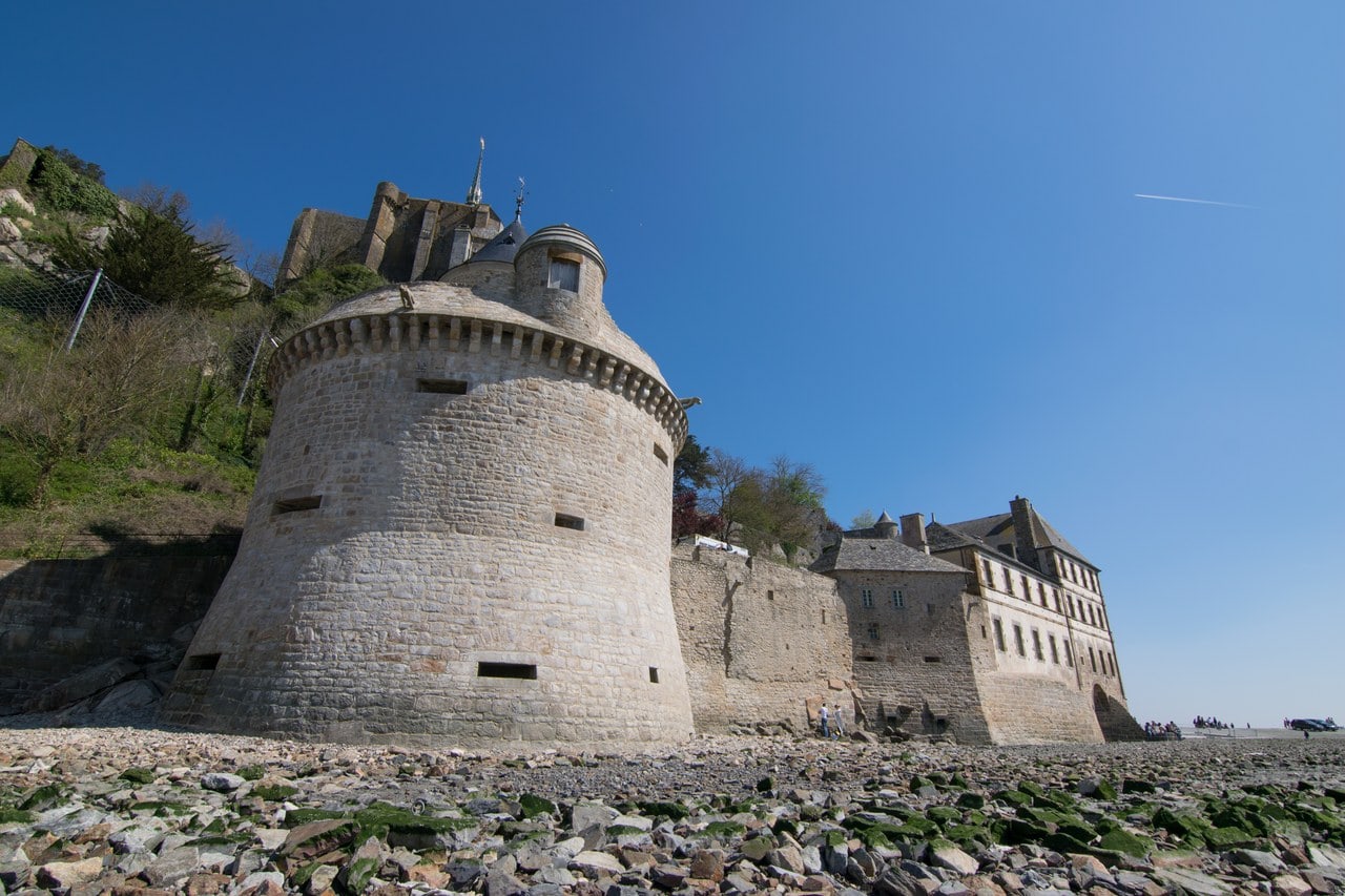 A large round tower with a battered stone base and low rectangular openings, a small turret on top, standing on rocks by the shore A large round tower with a battered stone base and low rectangular openings, a small turret on top, standing on rocks by the shore
