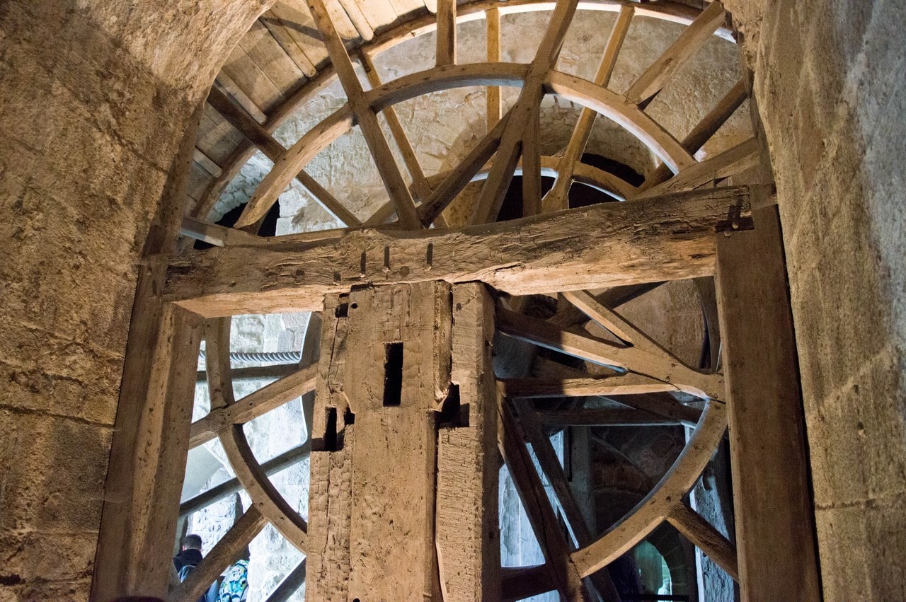 The great treadwheel at Mont-Saint-Michel seen from below through a stone arch, a drum of radiating wooden spokes and a curved rim wide enough for men to walk inside, carried on a massive timber axle, with visitors small beyond it. The wheel dates from 1818 and is a replica of the medieval machines it replaced. The great treadwheel at Mont-Saint-Michel seen from below through a stone arch, a drum of radiating wooden spokes and a curved rim wide enough for men to walk inside, carried on a massive timber axle, with visitors small beyond it. The wheel dates from 1818 and is a replica of the medieval machines it replaced.