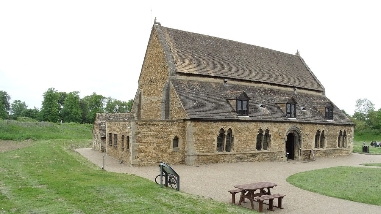 A single stone hall building with a tiled roof standing by itself on mown grass, with earthworks and trees behind it and no other castle buildings in the frame. A single stone hall building with a tiled roof standing by itself on mown grass, with earthworks and trees behind it and no other castle buildings in the frame.