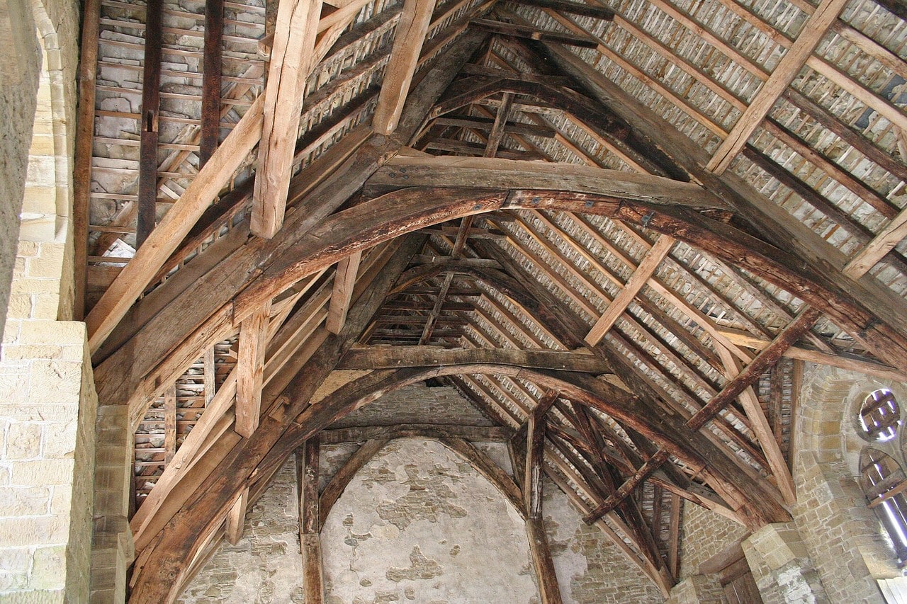 Looking up into an open medieval roof: curved cruck blades rise to meet collars and purlins, with the underside of the rafters visible above and no ceiling of any kind. Looking up into an open medieval roof: curved cruck blades rise to meet collars and purlins, with the underside of the rafters visible above and no ceiling of any kind.