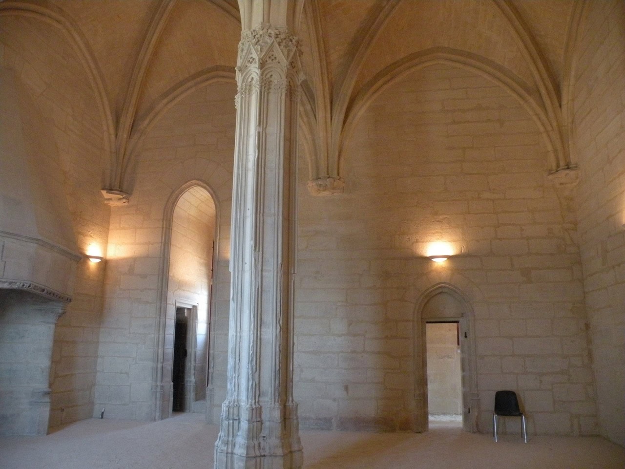 A tall vaulted room inside the donjon at Vincennes, its ribs springing from one slender carved pier in the middle of the floor, with two pointed-arched doorways cut through the pale stone walls.