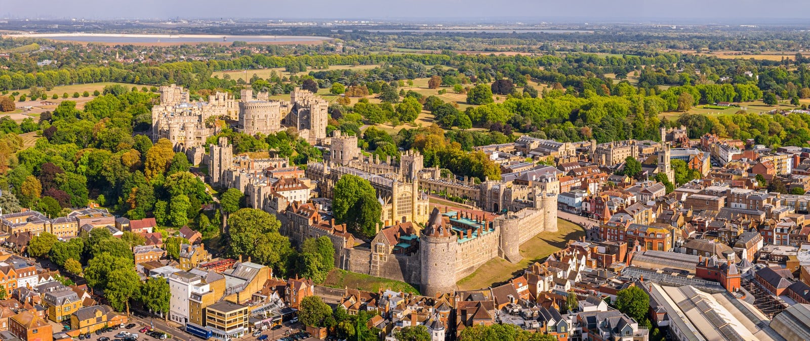 Oldest Castle in the World 1 An aerial view of Windsor Castle stretched along a low ridge, with a large round tower on a grassy mound at the center, a pinnacled Gothic chapel and a walled lower ward to one side, ranges of state apartments to the other, the town pressing up to the outer wall, and parkland behind.