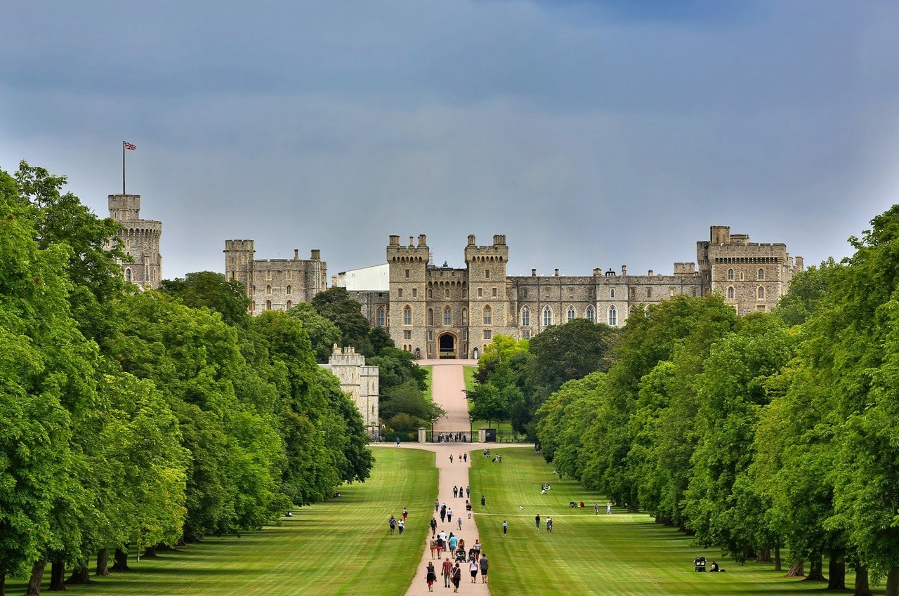 A long straight grass and gravel avenue between double rows of trees, with Windsor Castle small on the horizon at its far end. A long straight grass and gravel avenue between double rows of trees, with Windsor Castle small on the horizon at its far end.