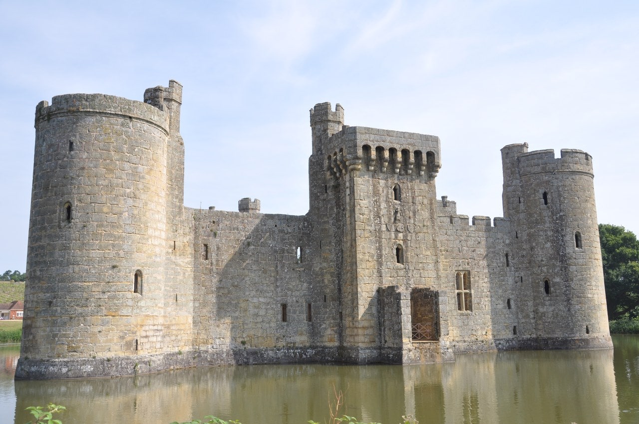 Square machicolated tower between two round corner towers at Bodiam Castle, rising from the moat