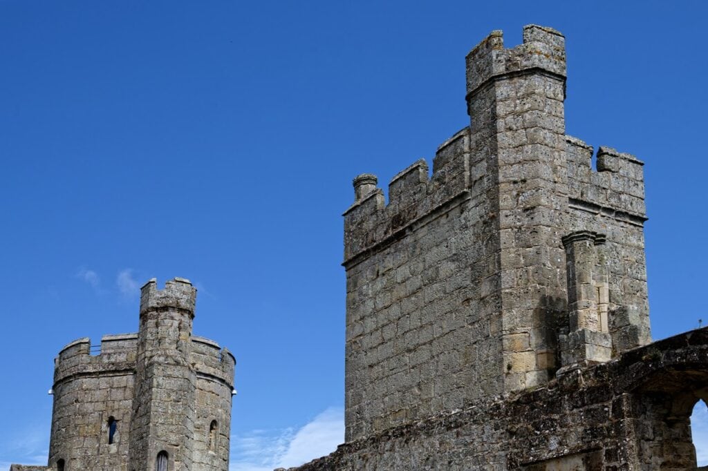Square crenellated tower at Bodiam Castle with a round corner tower behind under a clear sky