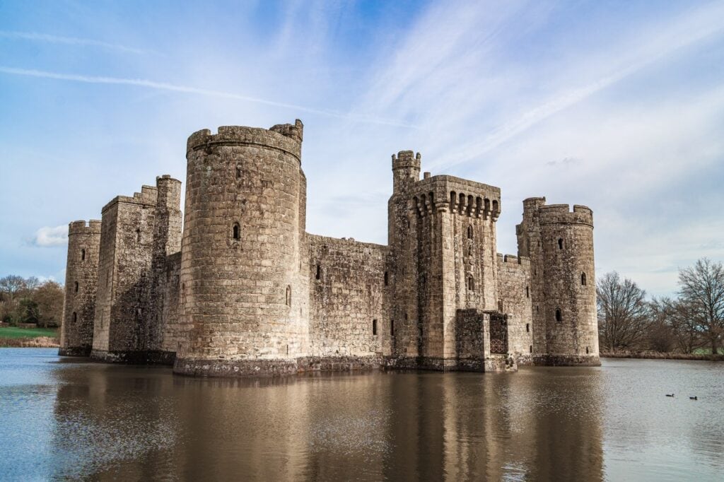 Bodiam Castle seen across its moat from the south-west, round corner towers reflected in still water