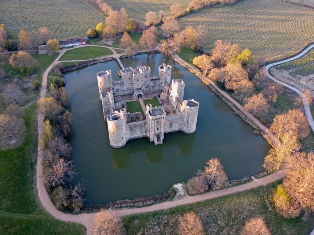 Aerial view of Bodiam Castle in its moat in low evening light, the surrounding trees bare or just coming into leaf