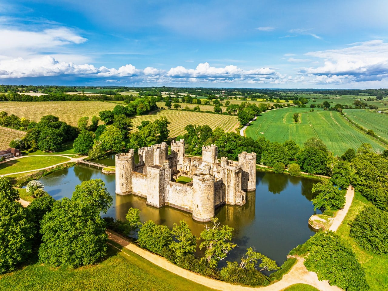 Oblique aerial of Bodiam Castle in its rectangular moat with paths and trees around the water