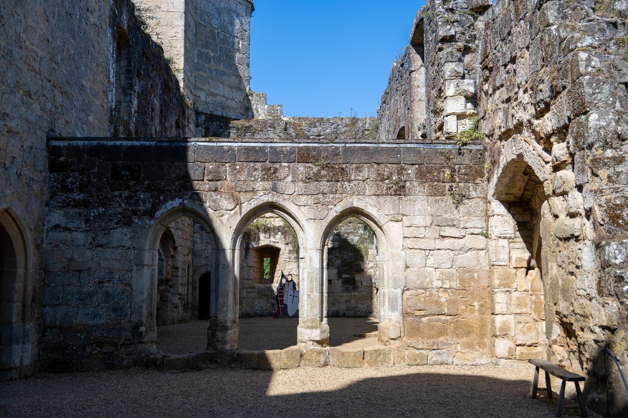 Three pointed arches of the screens passage inside the roofless south range at Bodiam Castle, doorways visible through them and a bench beside them