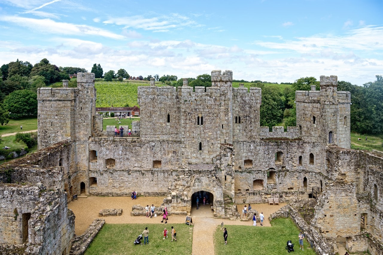 Wide view of the grass courtyard of Bodiam Castle with visitors crossing it, looking north to the roofless north range and the inner face of the gatehouse