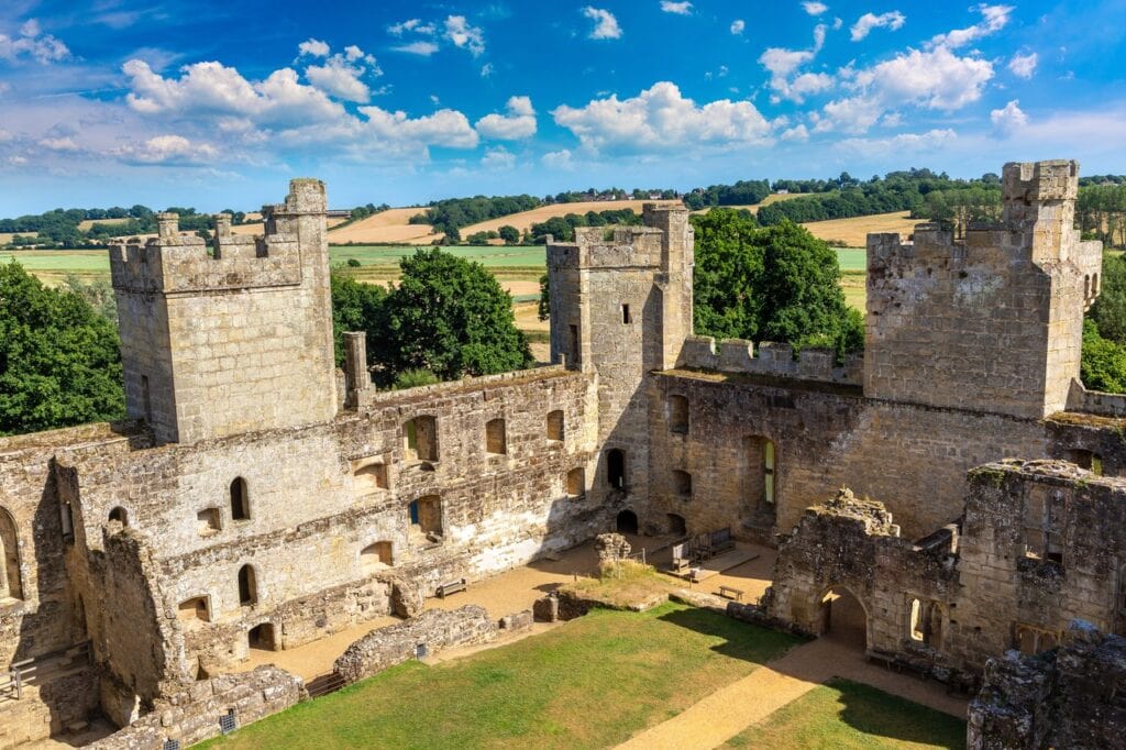 Elevated view across the Bodiam Castle courtyard to roofless range walls pierced by two floors of windows, three towers rising behind