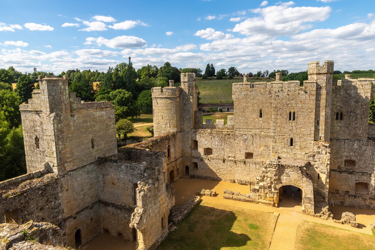Elevated view across the courtyard of Bodiam Castle to the inner face of the gatehouse, standing walls of the west range at left, a round corner tower between them and a lawn below