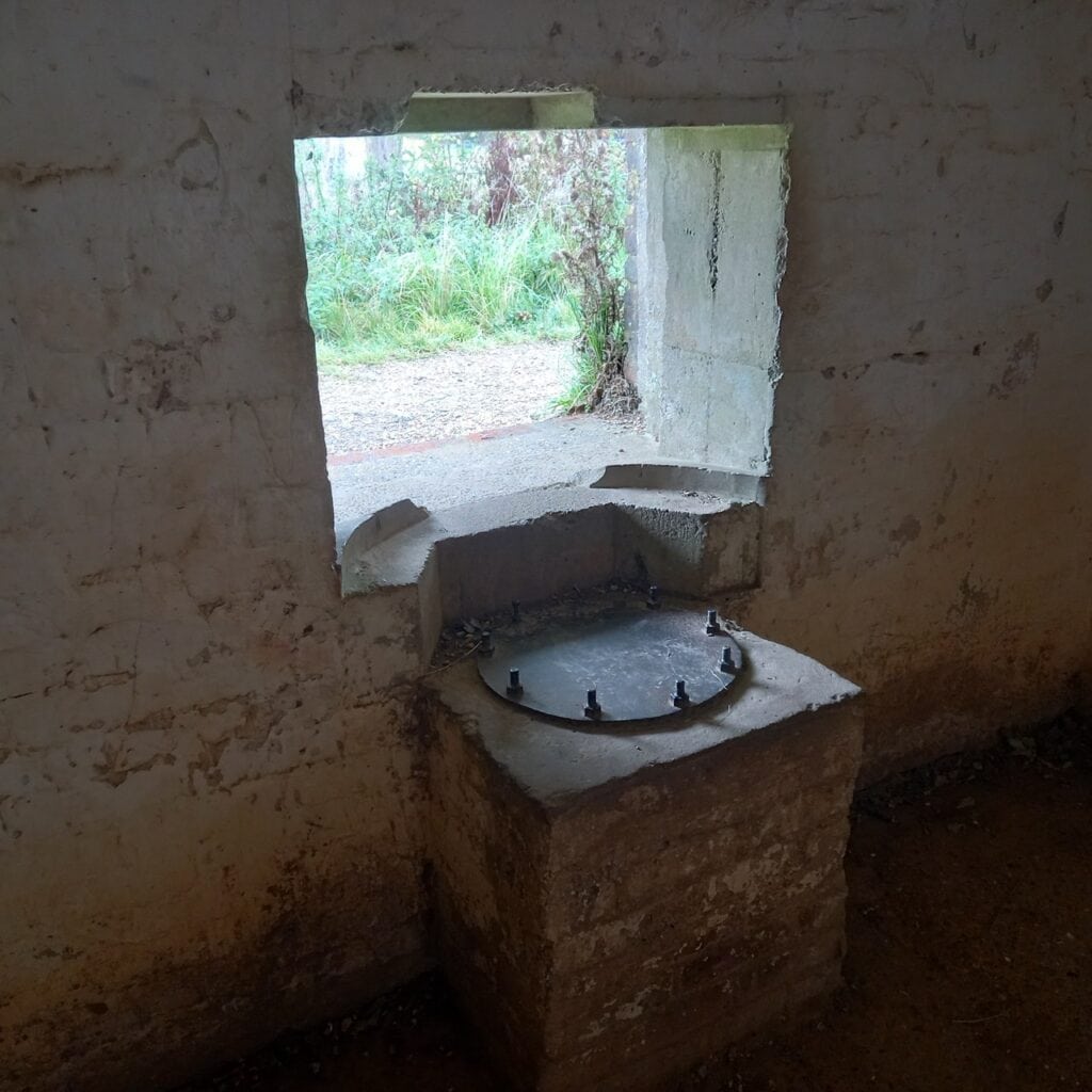 Whitewashed concrete interior of a Second World War pillbox with an embrasure and a gun mounting