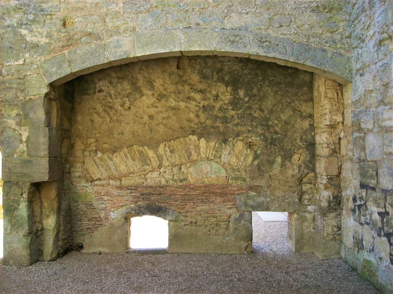 Wide segmental stone fireplace arch in the kitchen at Bodiam Castle, two small openings in the back wall