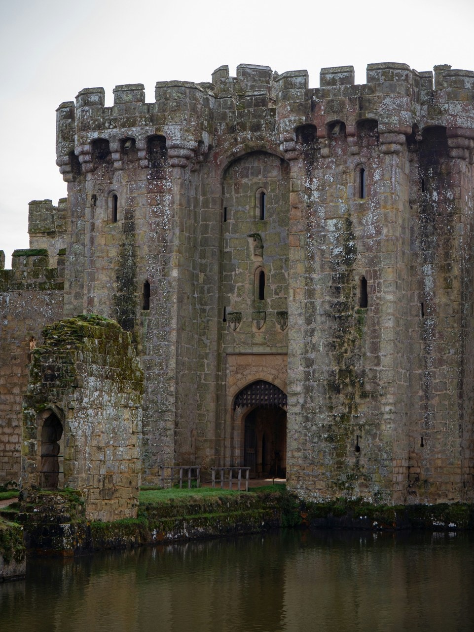 Twin-towered north gatehouse of Bodiam Castle rising from the moat, machicolations along the parapet