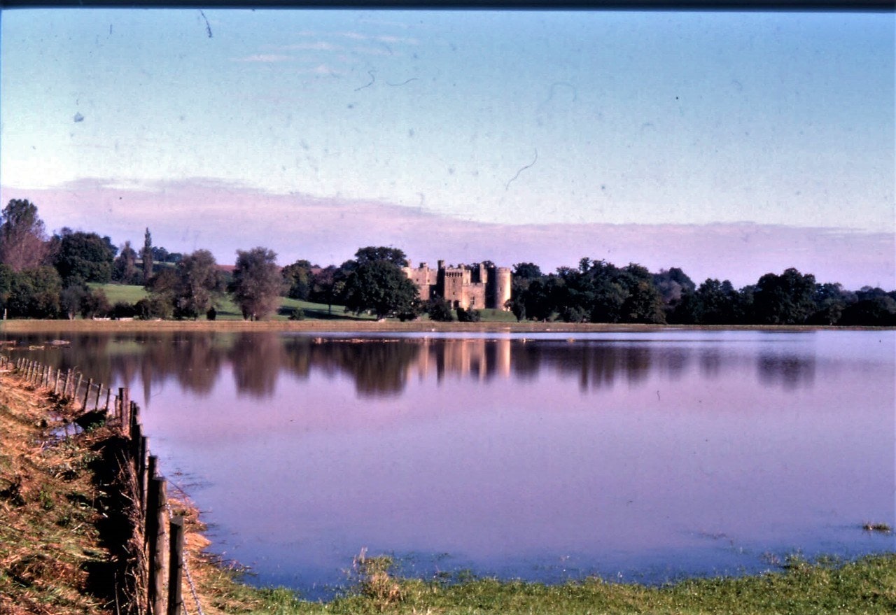 Bodiam Castle at dusk beyond a wide sheet of floodwater covering the valley fields