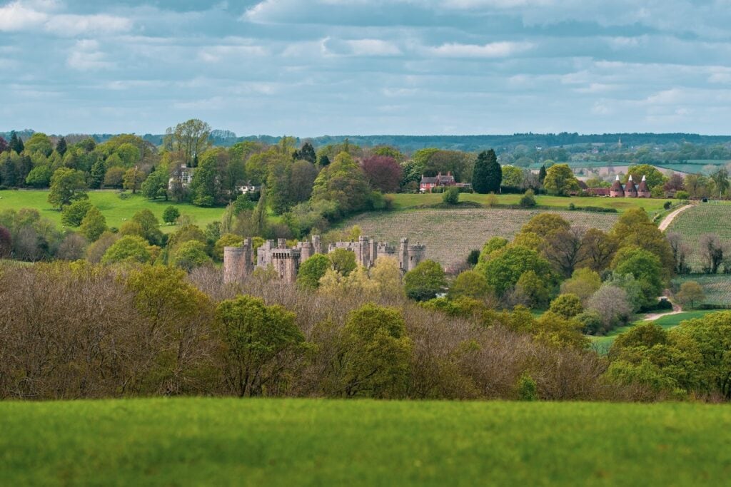 Distant view of Bodiam Castle in a wooded valley seen from rising farmland