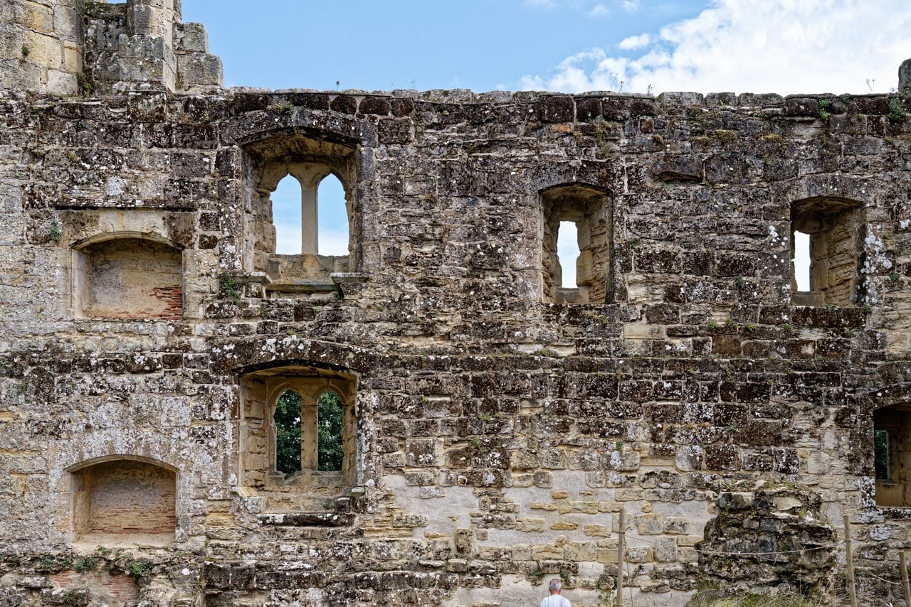 Roofless inner face of the curtain at Bodiam Castle pierced by two-light and single-light windows at two levels, sky and trees visible through them