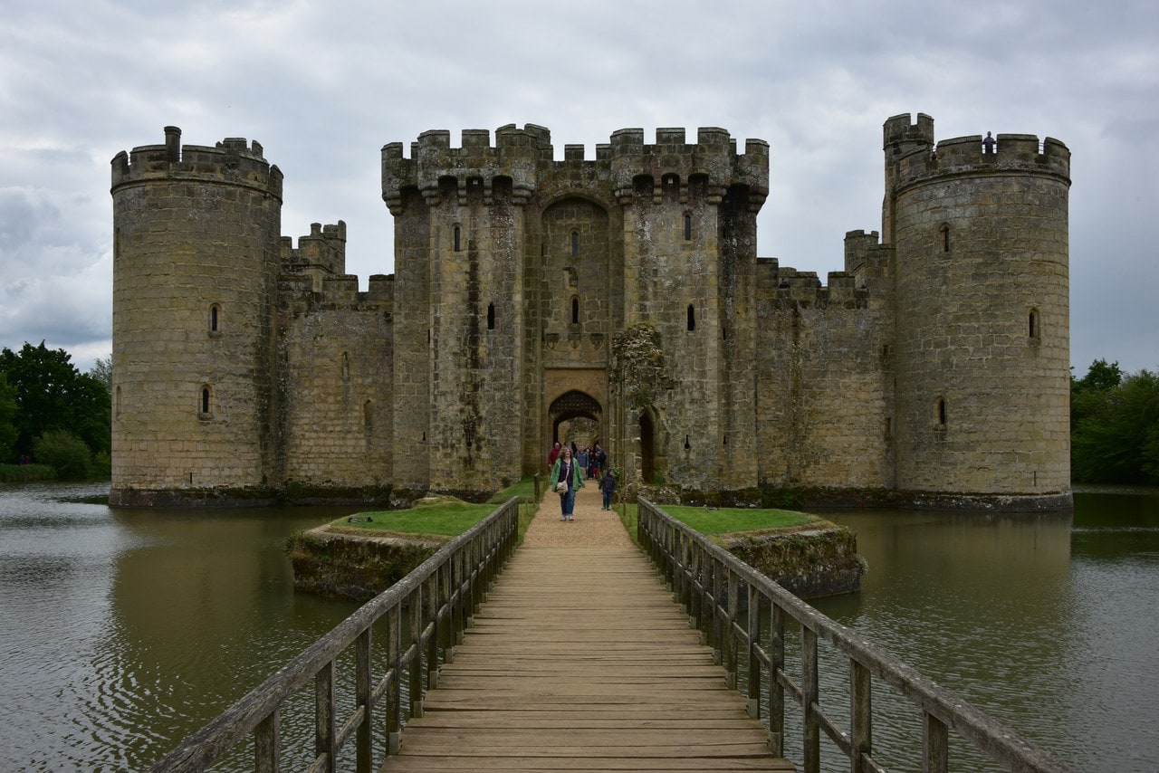 People walking across a timber bridge towards the gatehouse of Bodiam Castle