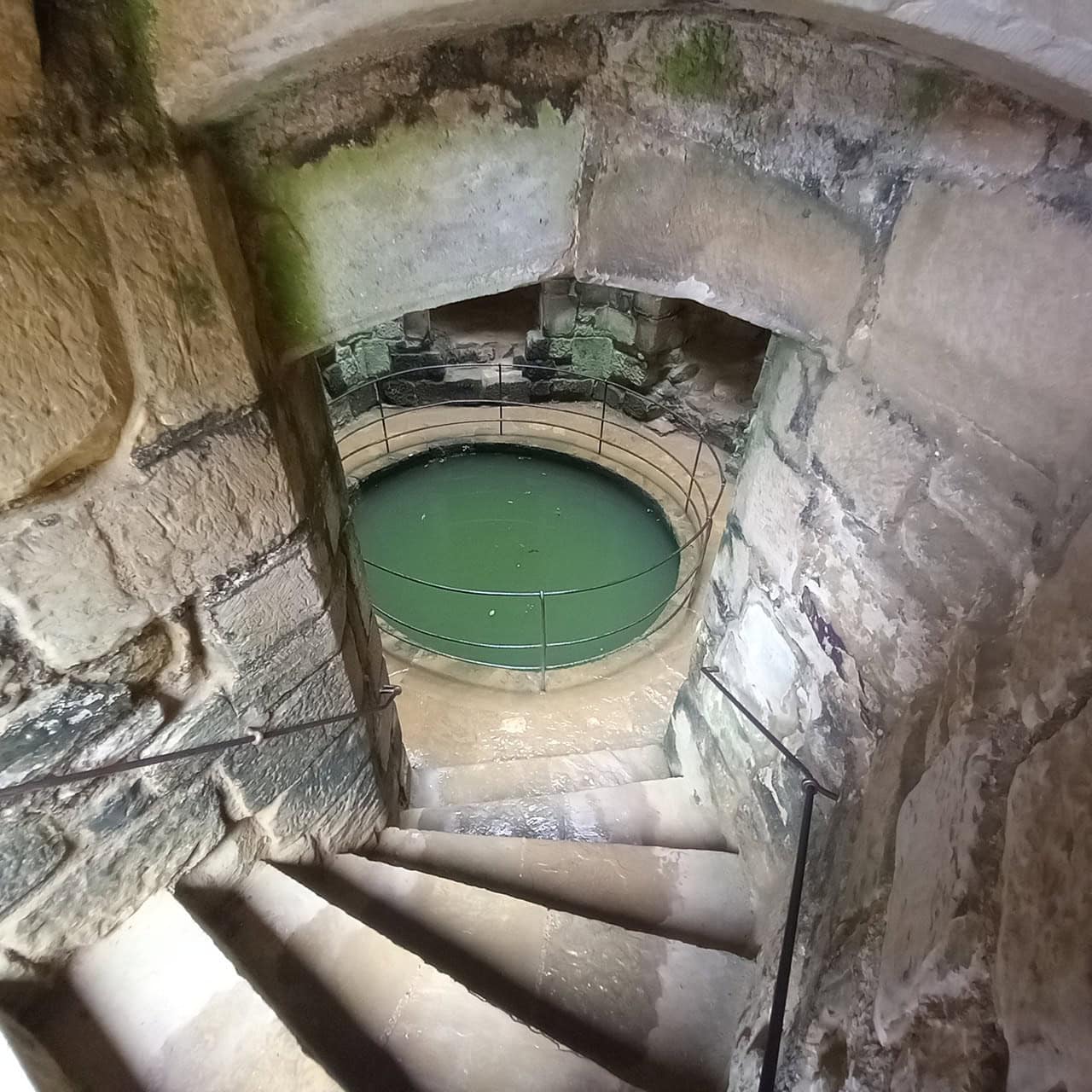 Circular stone well shaft holding green water inside a tower at Bodiam Castle, steps curving past it