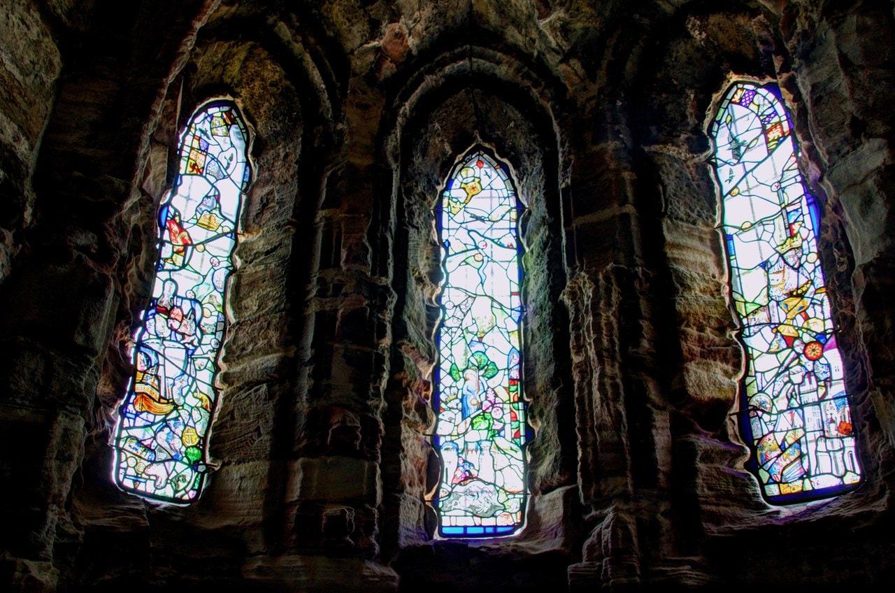 Three tall pointed lancet windows in a dark stone apse, filled with brightly colored modern stained glass.