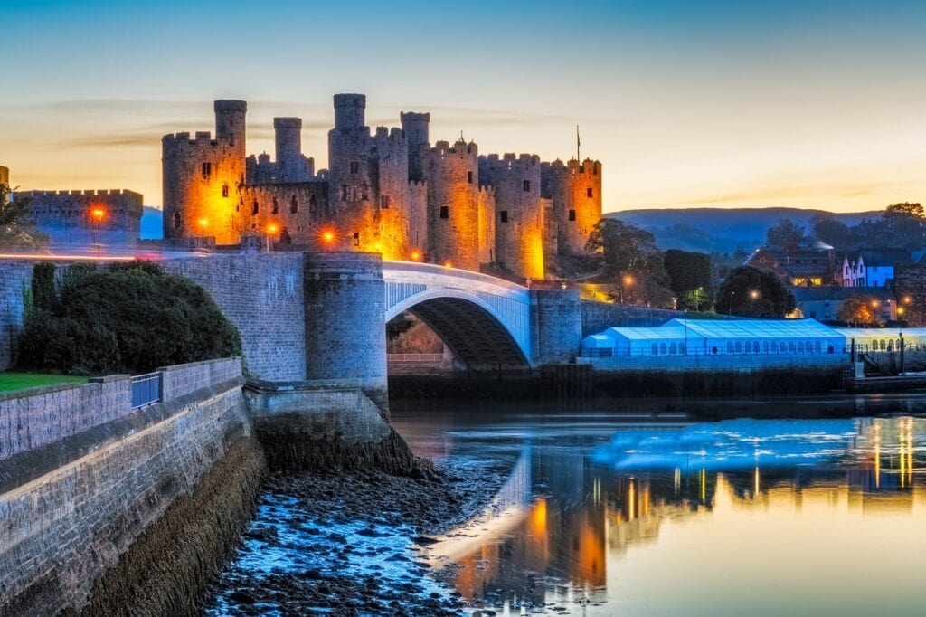 Conwy Castle floodlit at dusk above the road bridge, lights reflected in the river