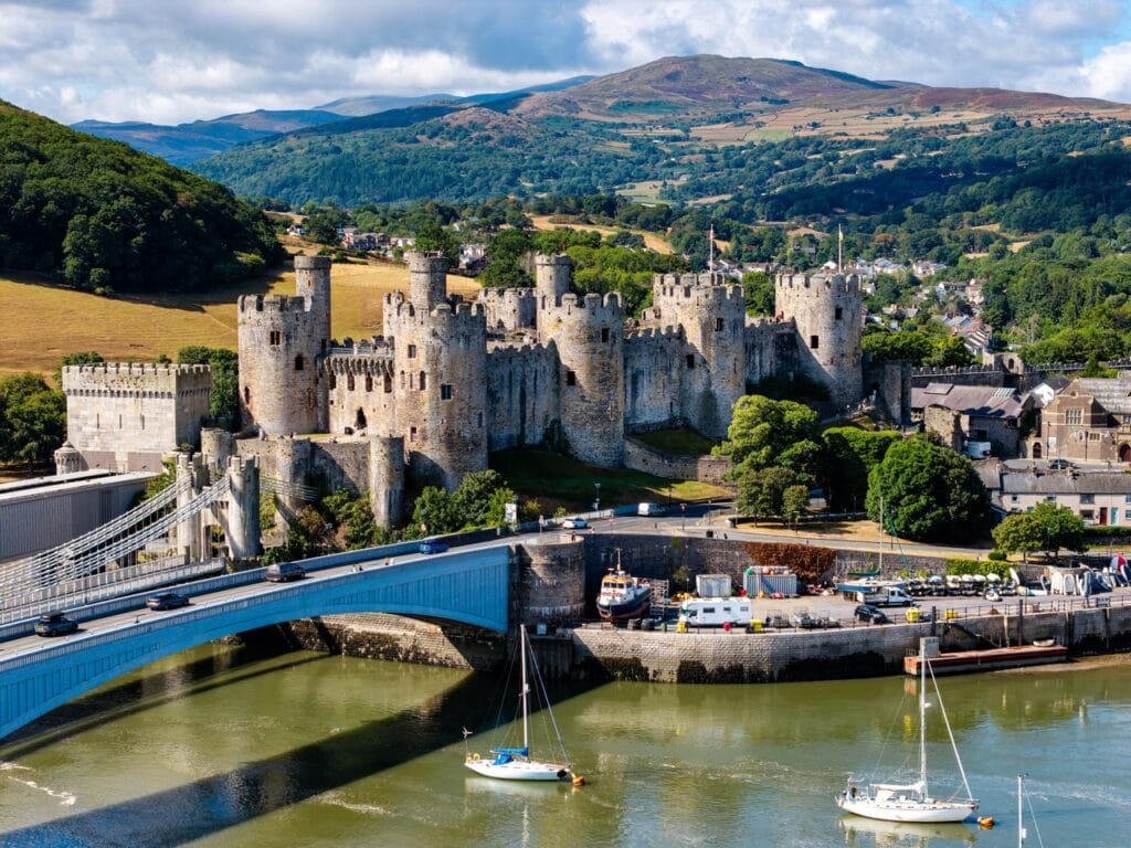 Conwy Castle above the quay and road bridge, seen from over the river with wooded hills behind