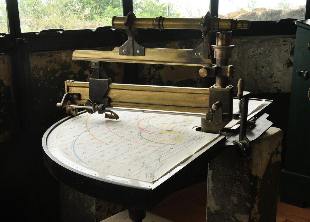 Dover Castle 11 A brass optical instrument on a pivoted bar over a semicircular graduated table marked with curved lines, in a dark room.