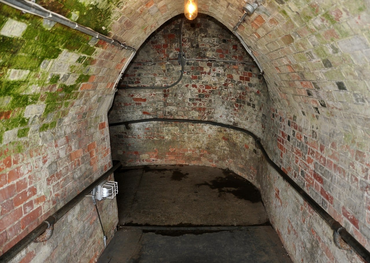 A brick barrel-vaulted tunnel with a cable run along the wall, lit by a single lamp. A brick barrel-vaulted tunnel with a cable run along the wall, lit by a single lamp.