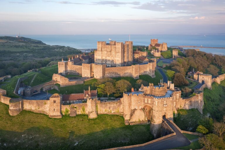 Home 8 Dover Castle from the air in low evening light, the square Great Tower at the center of its curtain walls, with the Channel behind.