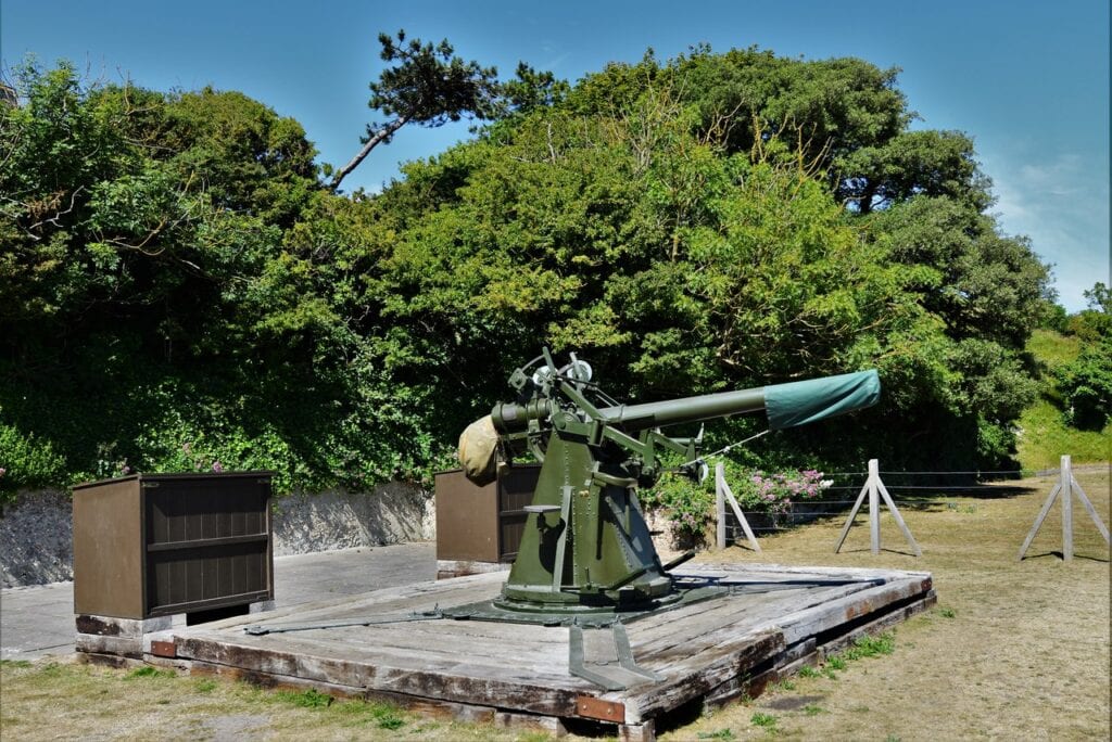 Dover Castle 9 A green anti-aircraft gun on a concrete platform, its long barrel raised against a screen of trees.