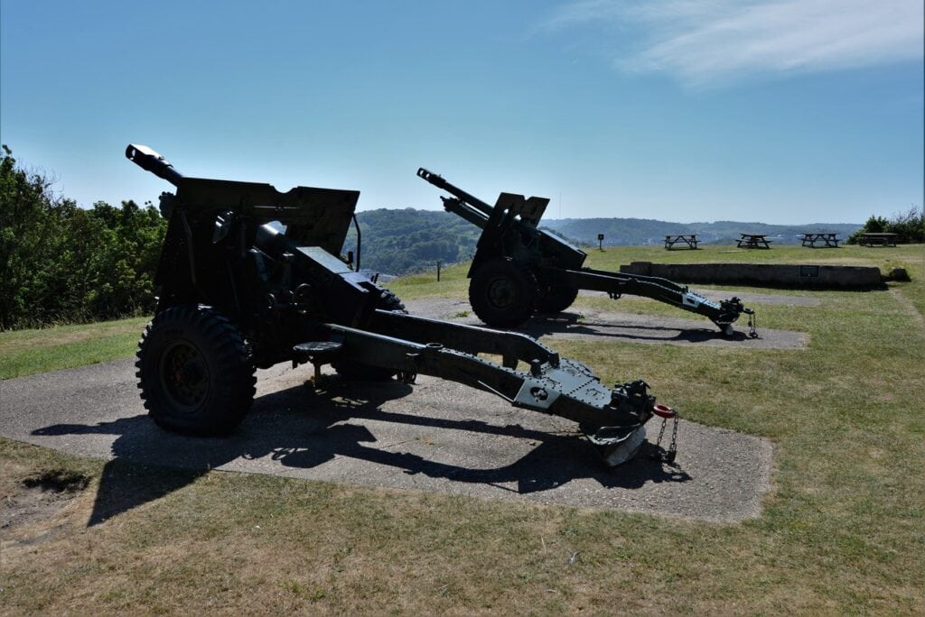 Dover Castle 8 Two field guns with split trails standing on concrete pads on open grass, with wooded hills behind.