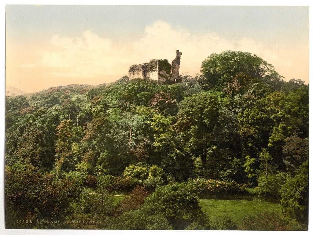Why Are English Castles in Ruins? 6 A colored photochrom print of a wooded hillside with the broken upper walls of a stone keep standing clear above the trees, and a meadow in the foreground.