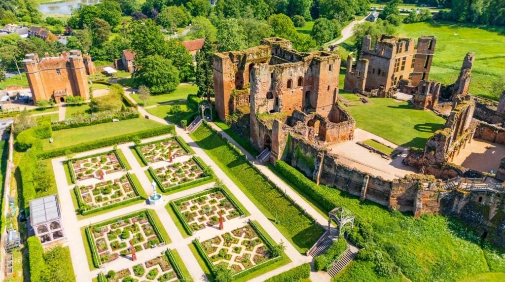 Kenilworth Castle 13 Aerial view over the Elizabethan garden: square beds with intricate low hedging and fences around a white central fountain, a latticed arbor on the terrace steps, the red sandstone Great Tower and roofless ranges beside them, and the square Leicester's Gatehouse with corner turrets at the upper left.