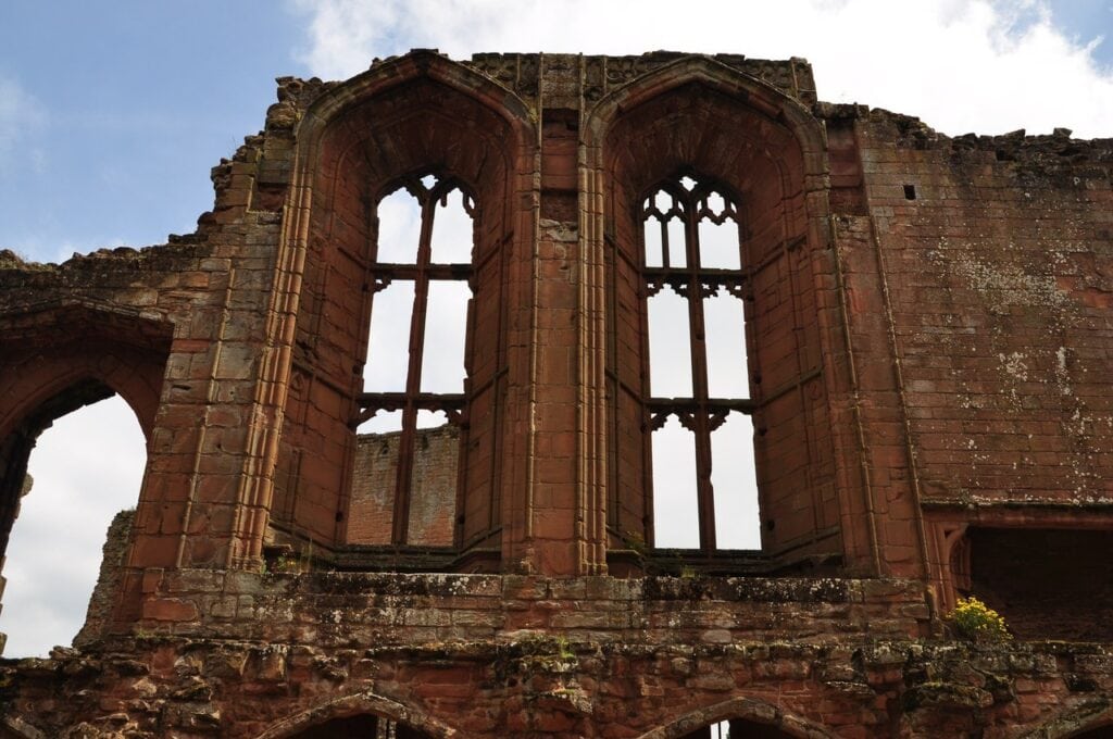 Kenilworth Castle 5 Two tall pointed window openings with stone mullions and tracery, set in deep molded arches in a red sandstone wall, seen against the sky.