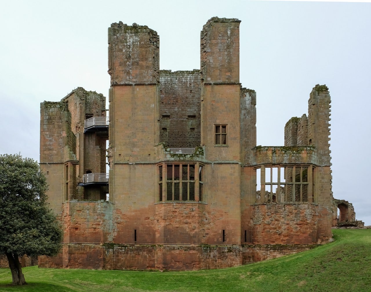 The ruined shell of Leicester's Building, a tall block of weathered red sandstone with large mullioned window openings and projecting bays, with two modern steel viewing platforms with railings inside the walls at the left. The ruined shell of Leicester's Building, a tall block of weathered red sandstone with large mullioned window openings and projecting bays, with two modern steel viewing platforms with railings inside the walls at the left.