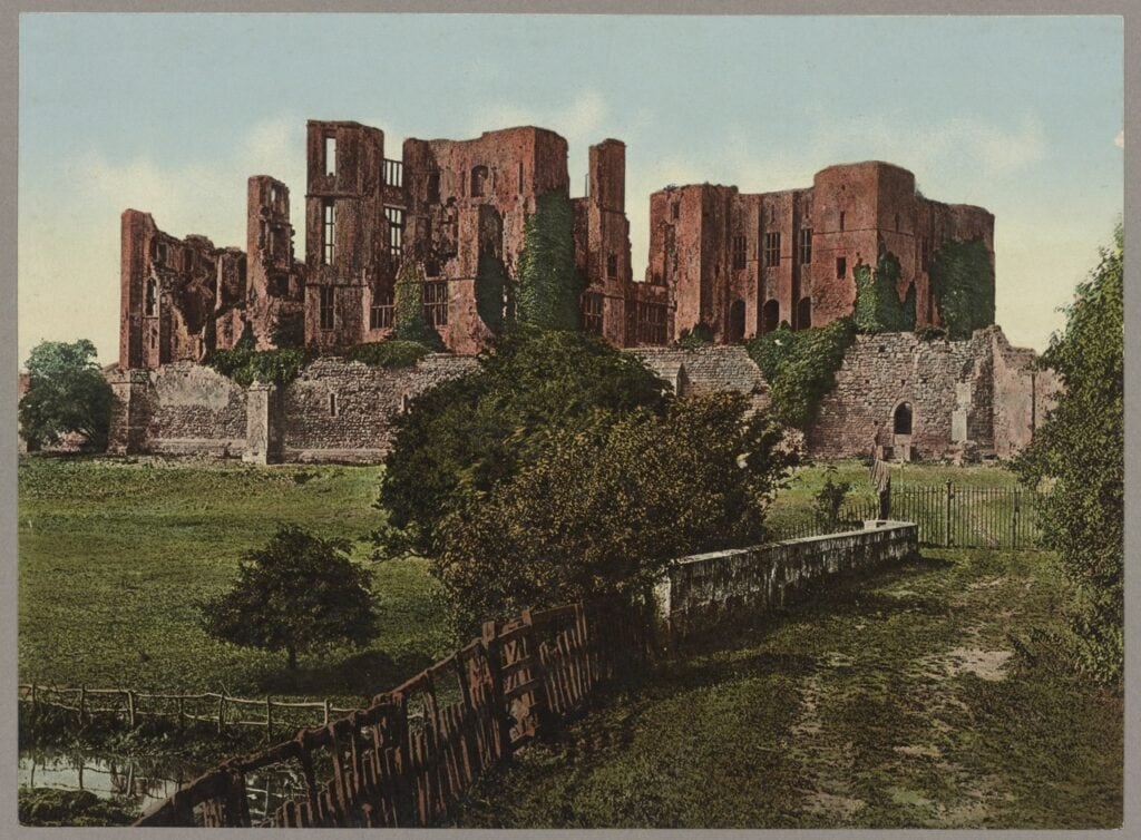Kenilworth Castle 2 A colored photochrom print of Kenilworth Castle's red ruins with ivy on the walls, a long wall in front, a fenced path and a low stone parapet leading in from the right foreground.
