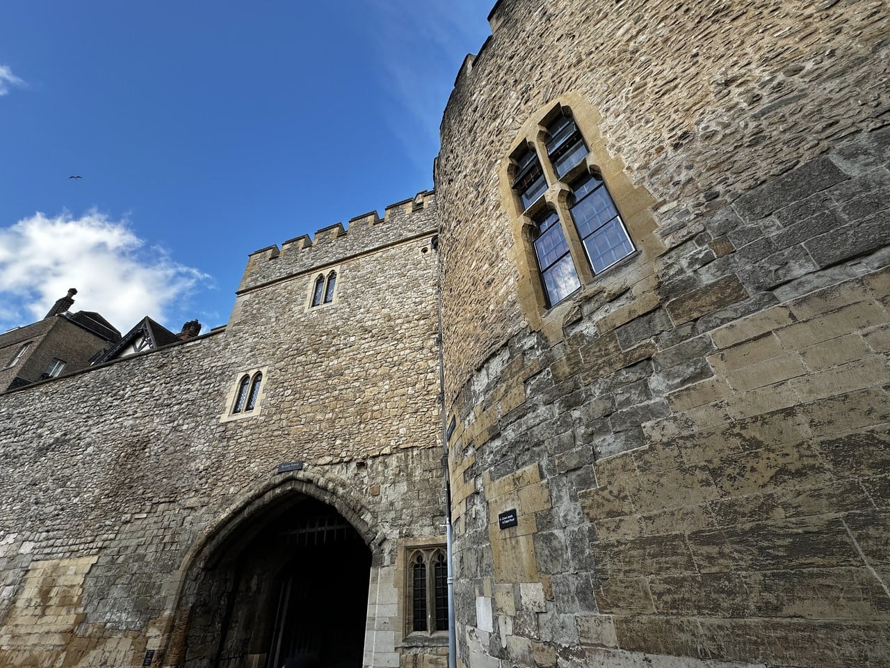 Looking up at a rectangular stone gate tower with a pointed arch over its passage, beside a round tower with a large traceried window.