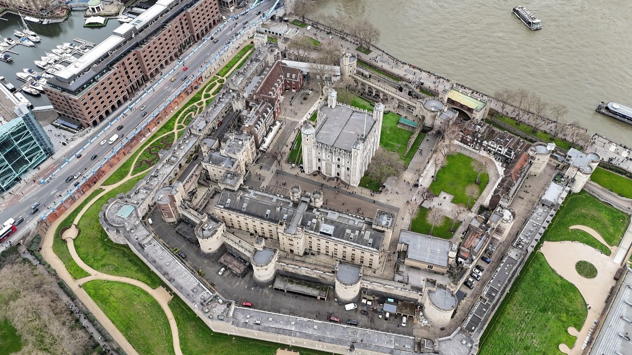 A high aerial view of the whole Tower of London: the White Tower at the center, the inner and outer walls with their towers, and the moat outside them.