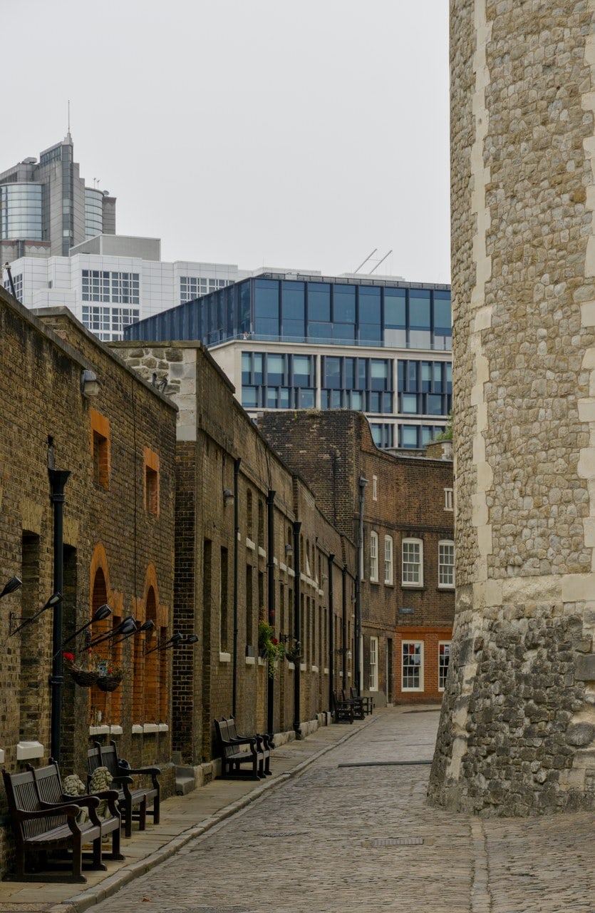 Mint Street, a cobbled lane between brick houses on the left and a stone curtain tower on the right, with modern buildings beyond.