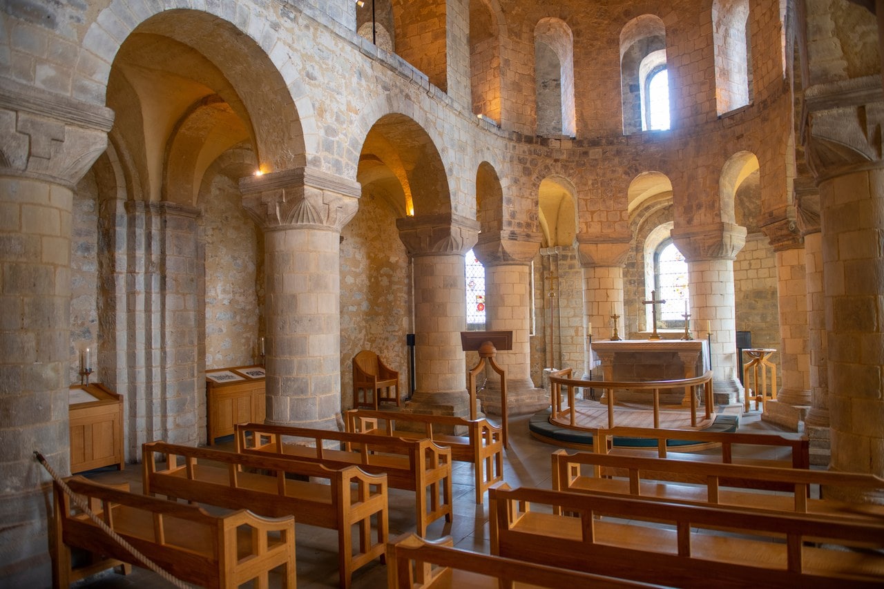 The interior of St John's Chapel, an arcade of round piers with carved capitals curving around the apse, with a gallery arcade above.
