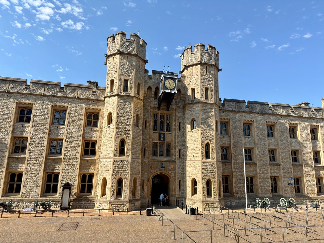 A Gothic Revival facade with two octagonal crenellated turrets flanking a central arched entrance labeled The Crown Jewels, with a sentry box and old guns on carriages in front.