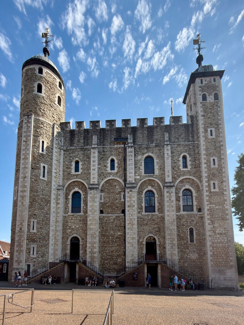 One face of the White Tower seen from a paved court, with a round turret at left, a square turret at right and two doors reached by short stairs.