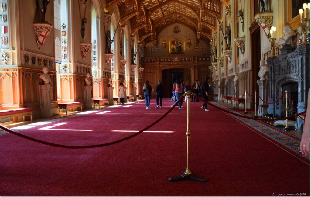 Windsor Castle 15 A long hall with a crimson carpet running its full length, an open timber roof overhead and heraldic shields along the walls