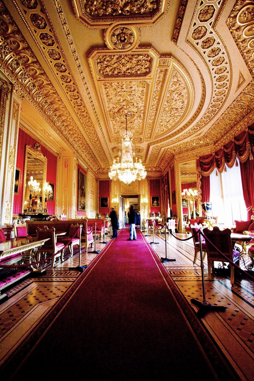 A richly gilded room with crimson silk walls, an elaborately modeled and gilded ceiling and a chandelier, seen looking down its length A richly gilded room with crimson silk walls, an elaborately modeled and gilded ceiling and a chandelier, seen looking down its length