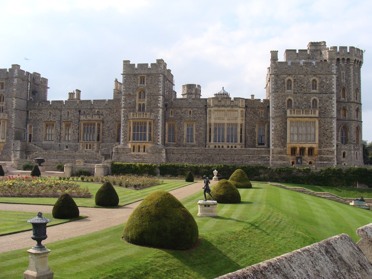 A formal garden of clipped topiary domes, gravel walks and a bronze statue on a plinth below a long battlemented range with tall windows, photographed in 2014 A formal garden of clipped topiary domes, gravel walks and a bronze statue on a plinth below a long battlemented range with tall windows, photographed in 2014